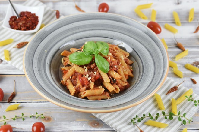 Penne Arrabiata mit Paprika und Oliven auf einem grauen Teller. Hintergrund hell.