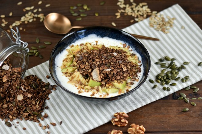 Schokoladen Granola in einer Schüssel mit Joghurt und Äpfeln.