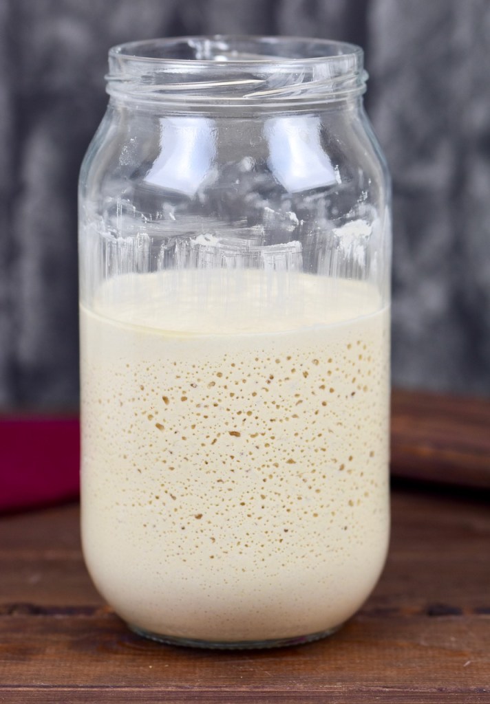 Glutenfreier Sauerteig im Glas. Man sieht die Bläschenbildung. Hintergrund dunkel.