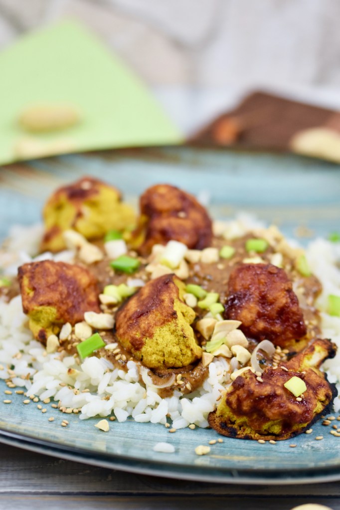 Knusprige Blumenkohlröschen mit Erdnusssauce und Reis, garniert mit Erdnüssen und Frühlingszwiebeln.