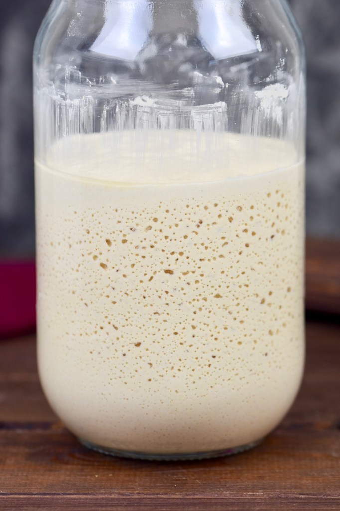 Glutenfreier Sauerteig im Glas. Man sieht die Bläschenbildung. Hintergrund dunkel.