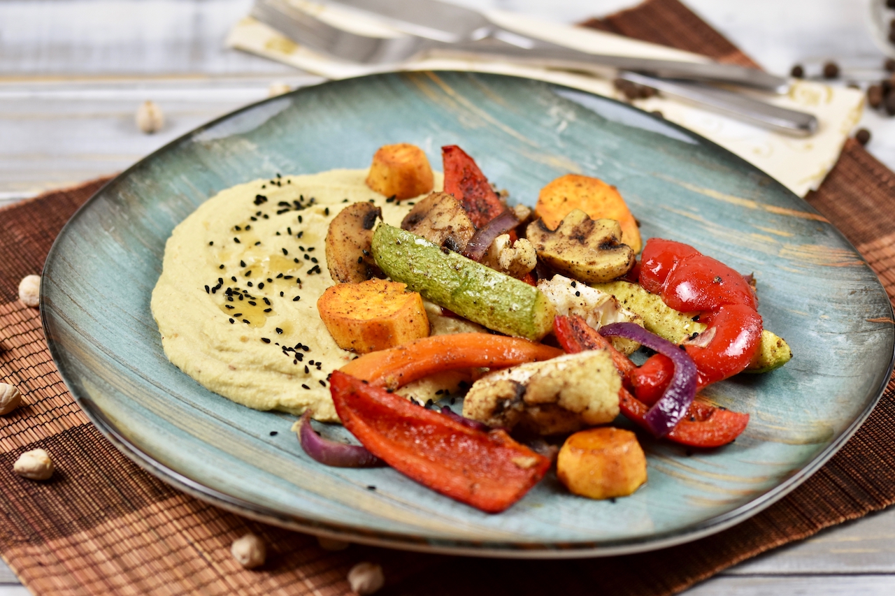 Hummus mit geröstetem Knoblauch und Ofengemüse auf türkisem Teller.