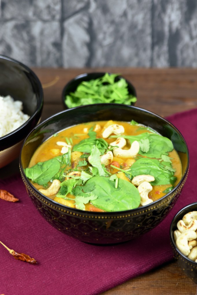 Kürbis-Curry mit Kokosmilch, Kichererbsen und Spinat in einer dunklen Schüssel.