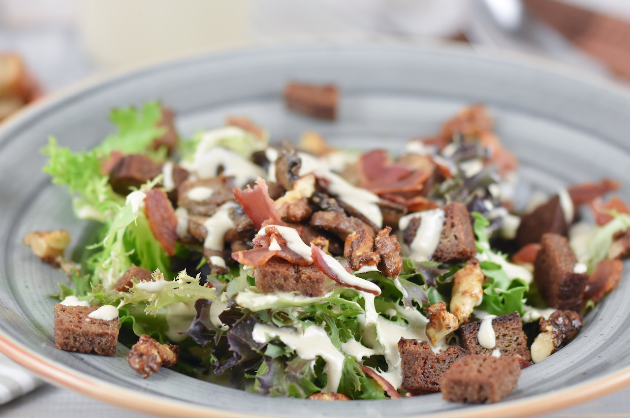 Veganer Caesar Salad mit Pilzen und Walnüssen auf grauem Teller. Hintergrund hell.