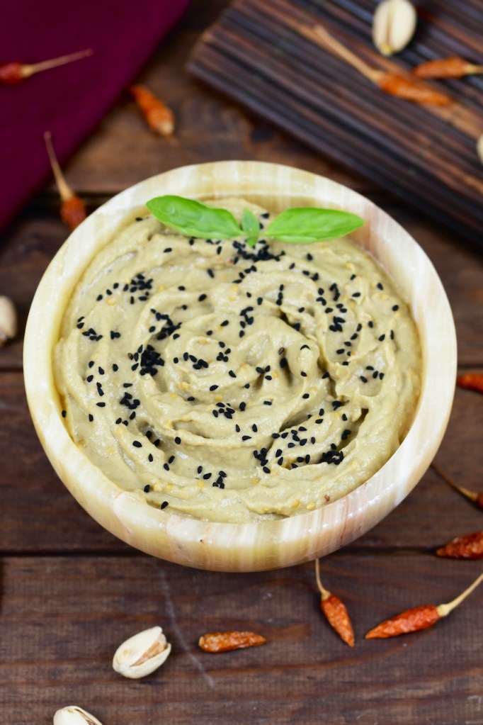 Orientalisches Mutabbal in einer Schale garniert mit Schwarzkümmelsamen und Basilikum. Hintergrund dunkel.