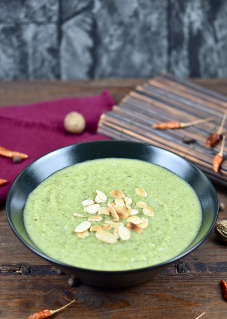 cremige Brokkolisuppe in schwarzer Schale, dekoriert mit Mandelplättchen. Hintergrund dunkel