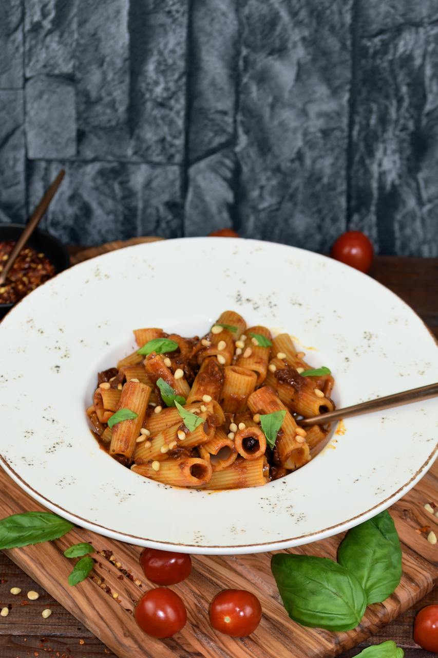 Pasta mit karamellisierten Zwiebeln auf weißem Teller. Hintergrund dunkel.