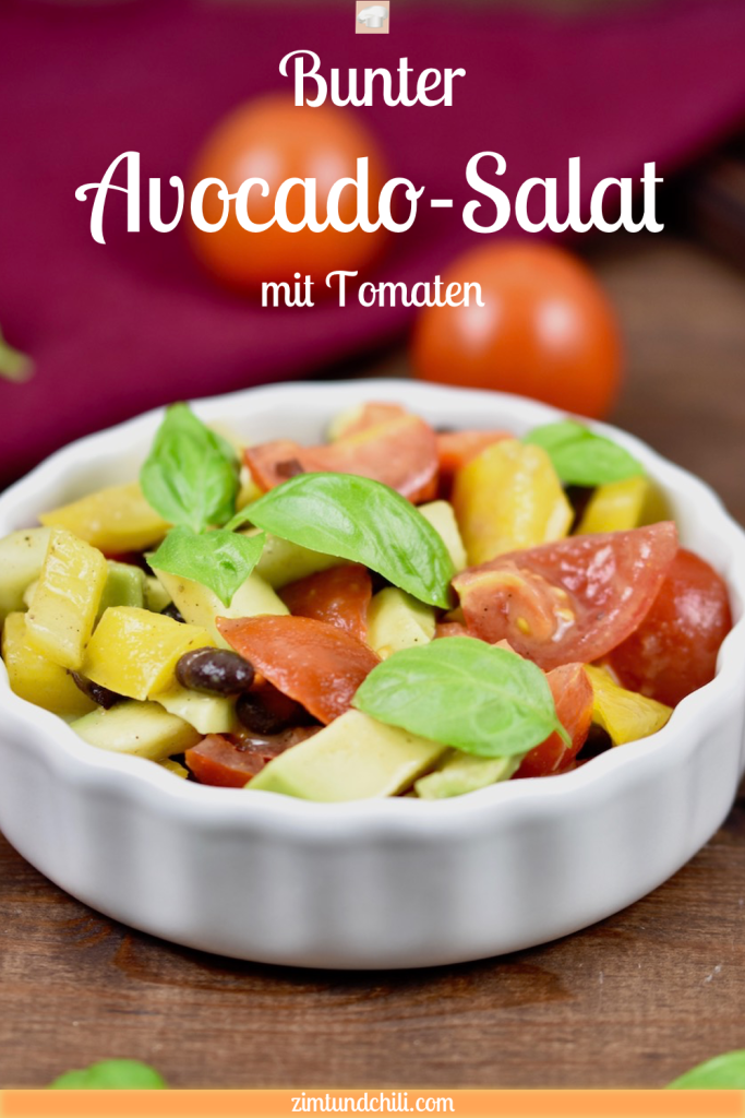 Bunter Avocado-Salat mit Tomaten in weißer Schale. Dekoriert mit Basilikum. Hintergrund dunkel. Bild beschriftet