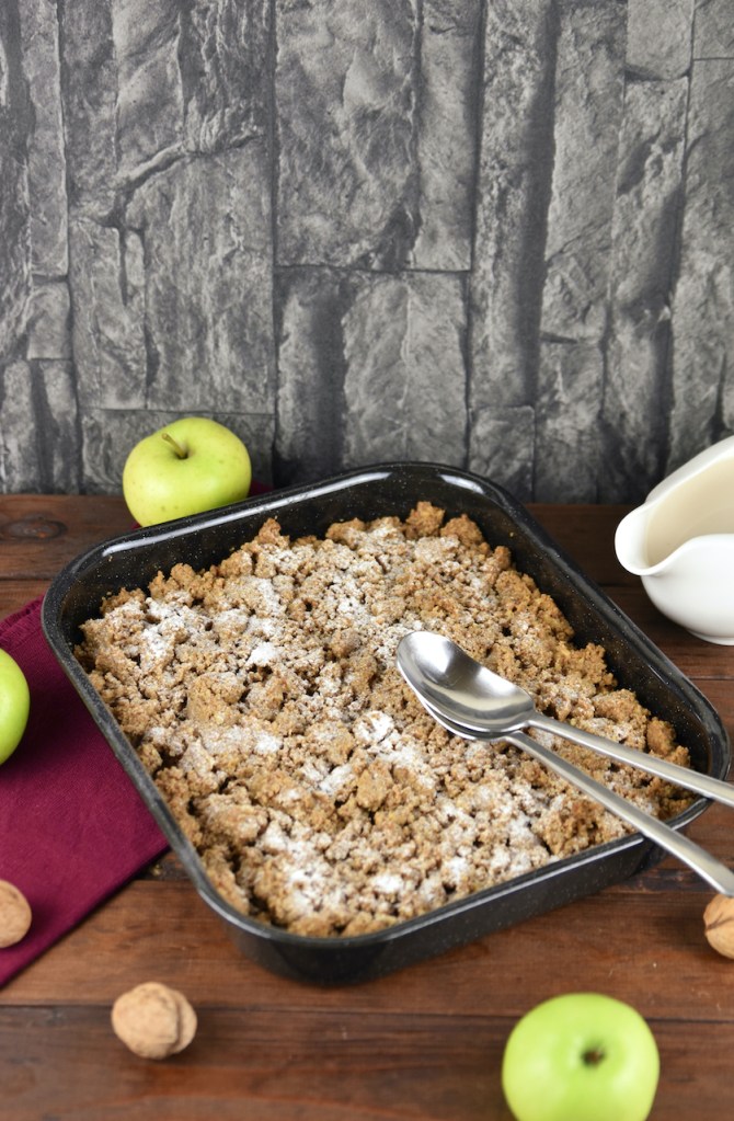 Apple Crumble mit Walnüssen und Haferflocken in einer Auflaufform. Hintergrund dunkel.