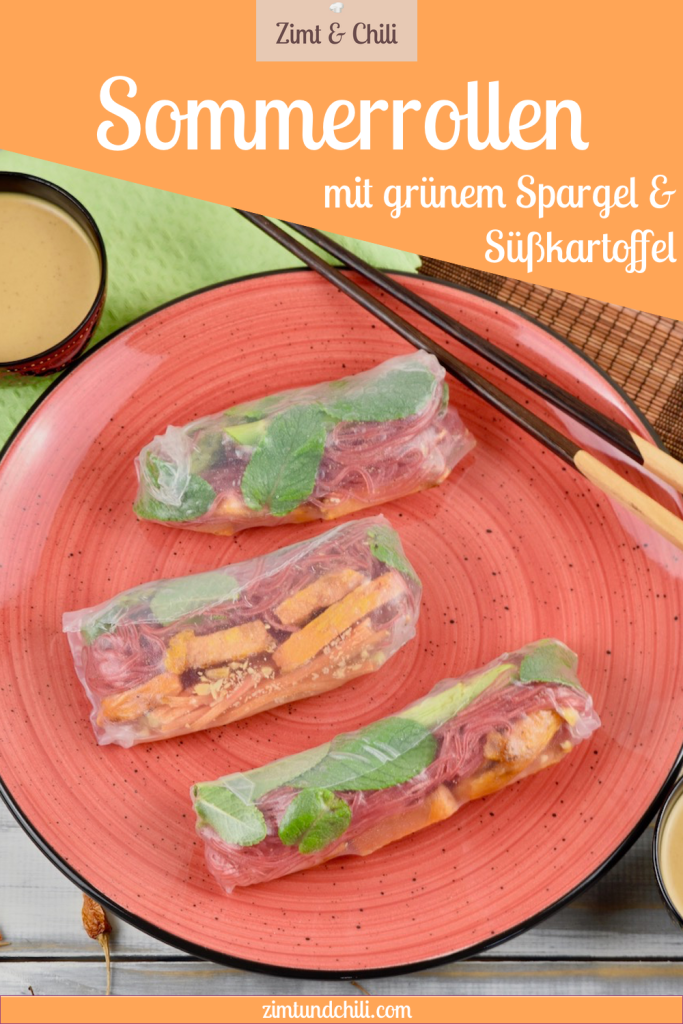 Drei Sommerrollen mit grünem Spargel und Süßkartoffel auf einem roten Teller. Auf dem Teller liegen auch Stäbchen. Im Hintergrund sieht man ein Schälchen mit Erdnusssauce. Beschrifteter Pin.