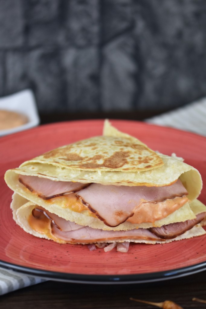 Reuben Sandwich-Tortilla Wrap auf rotem Teller. Hintergrund dunkel.