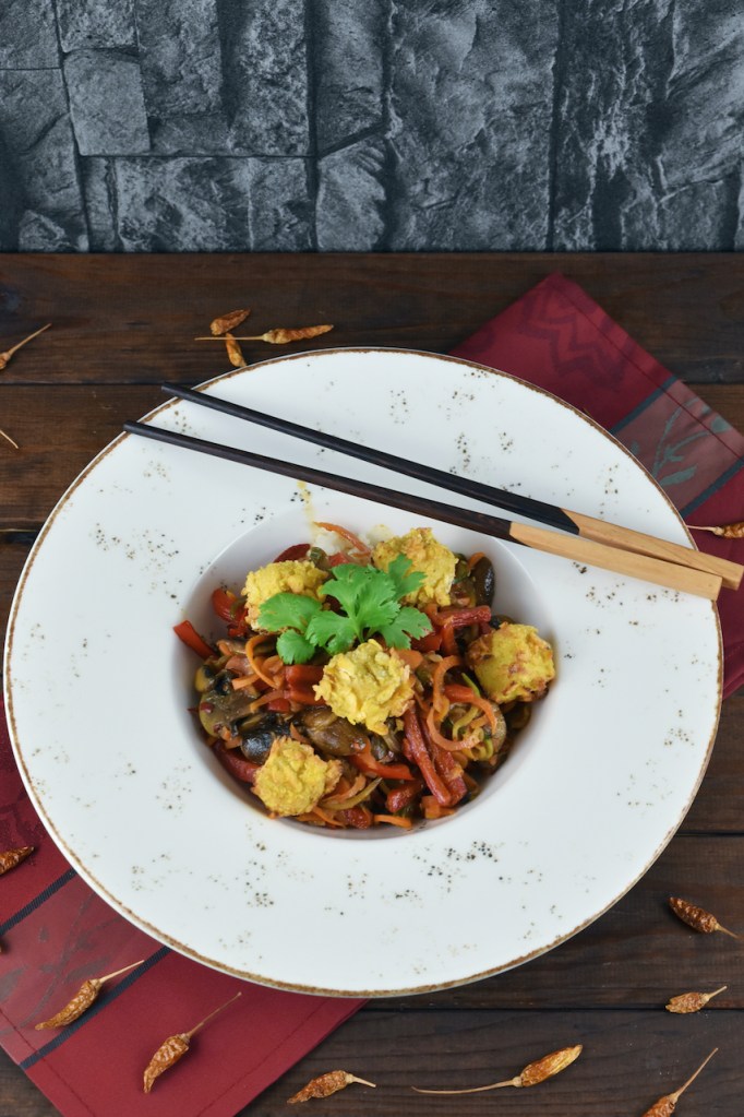 Asiatisches Wokgemüse mit knusprigem Tofu auf weißem Teller. Hintergrund dunkel.