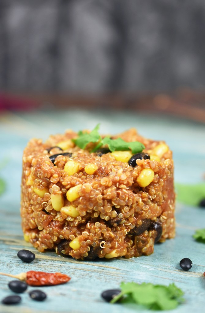 Quinoa-Pfanne auf mexikanische Art auf blauem Teller. Hintergrund dunkel.