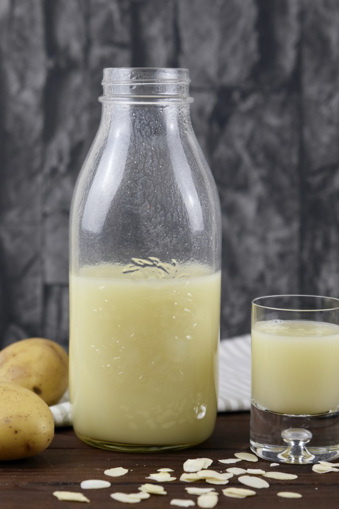 Vegane Milch aus Kartoffeln in einer Glasflasche und einem Glas. Hintergrund dunkel.