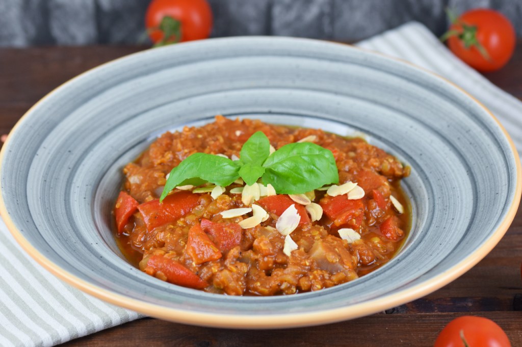 Italienischer Eintopf mit Tomaten, Paprika und Linsen in grauem Teller. Hintergrund dunkel.