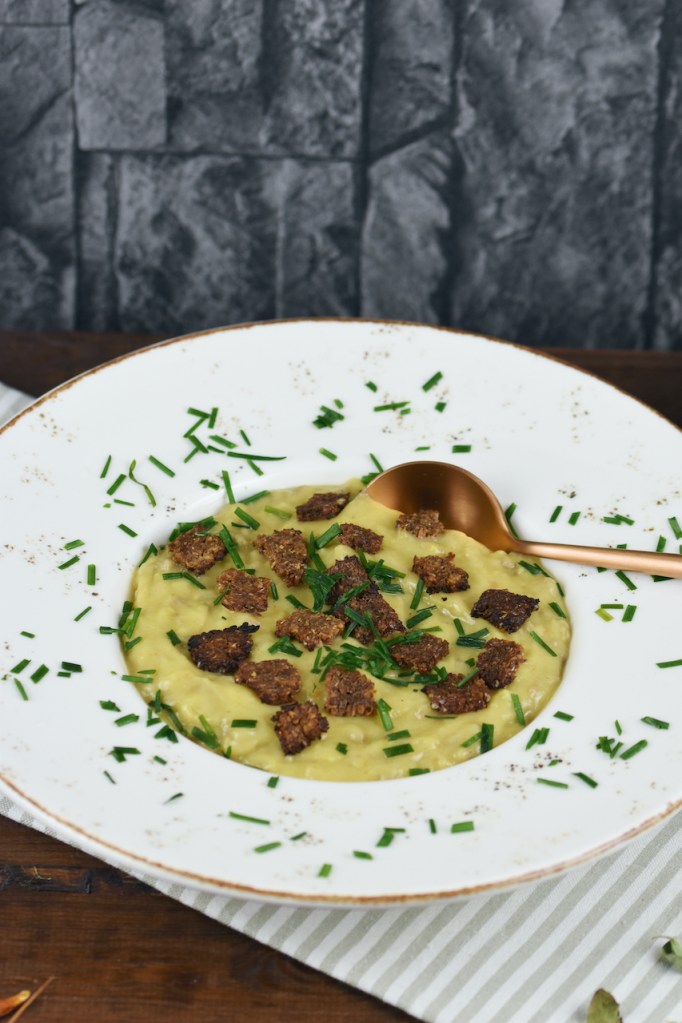 Cremige Kartoffel-Lauch-Suppe in einem weißen tiefen Teller. Hintergrund dunkel.