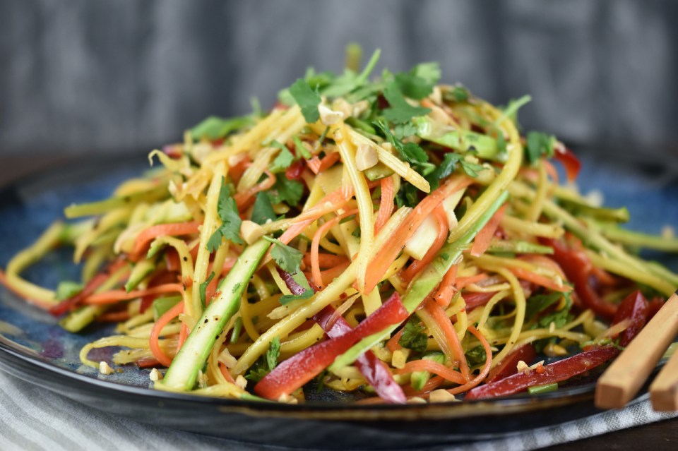 Thai Salat mit Mango und gerösteten Erdnüssen auf einem blauen Teller.
