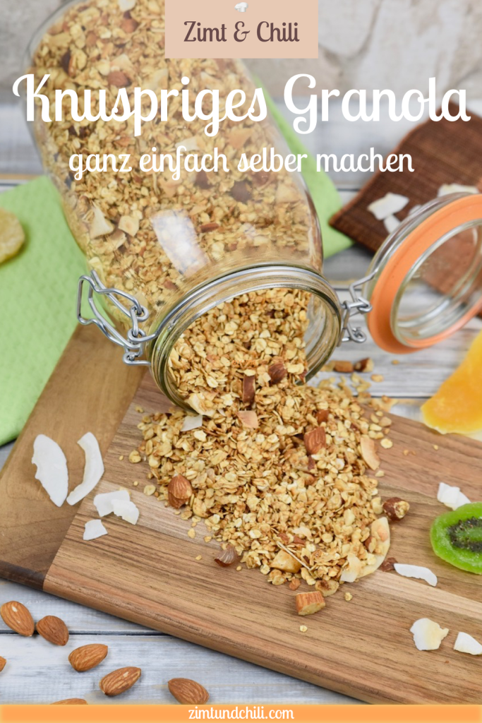 Knuspriges Granola, das aus einem liegenden Glas geschüttet wurde. Das ausgeschüttete Granola liegt auf einem Holzbrett und der Hintergrund ist hell. Beschrifteter Pin.