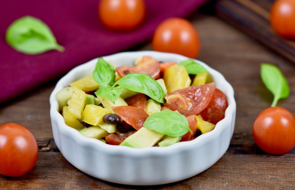 Bunter Avocado-Salat mit Tomaten in weißer Schale. Dekoriert mit Basilikum. Hintergrund dunkel
