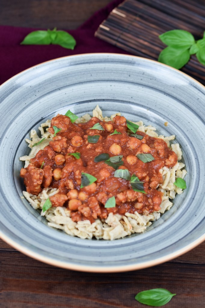 Pasta mit Salsiccia und Kichererbsen auf blauem Teller. Hintergrund dunkel.