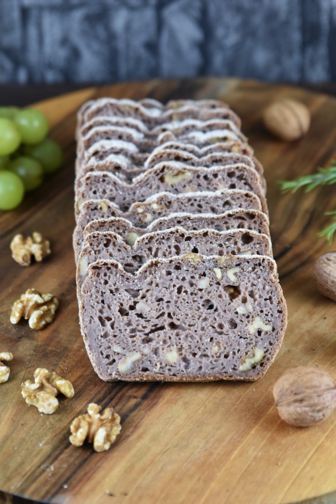 Glutenfreies Walnussbrot aufgeschnitten auf Holzbrett. Hintergrund dunkel.