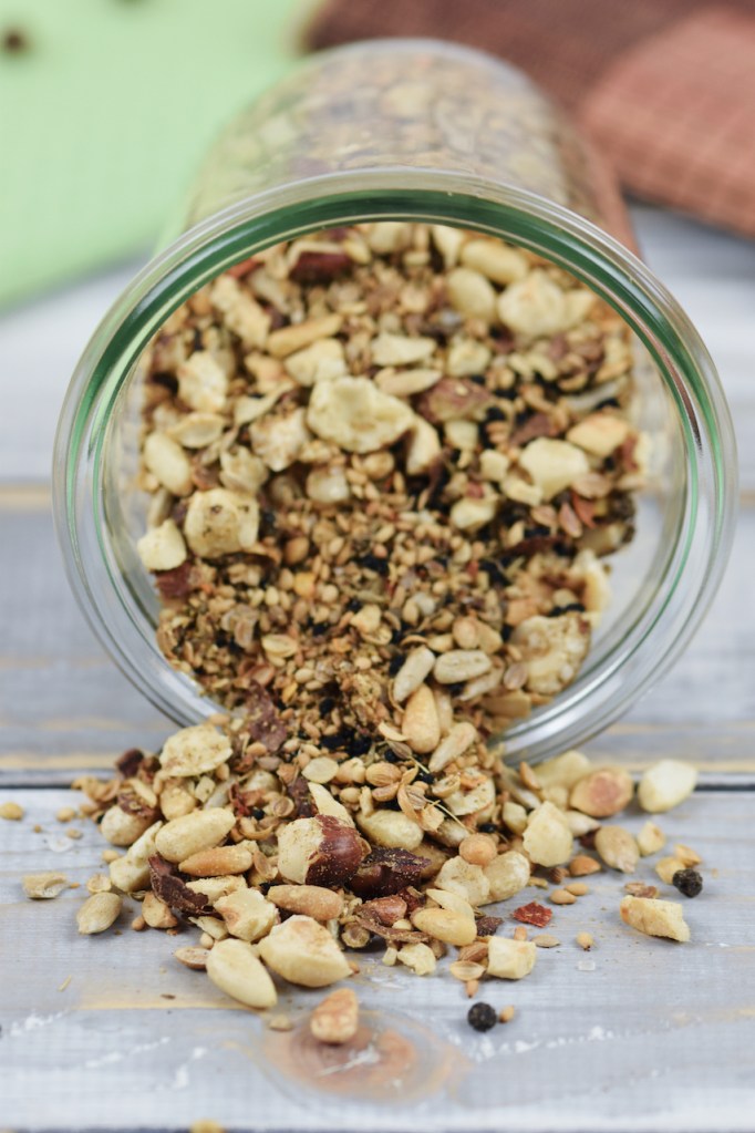 Dukkah selber gemacht in einem liegenden Glas. Etwas Dukkah ist herausgerutscht. Hintergrund hell.