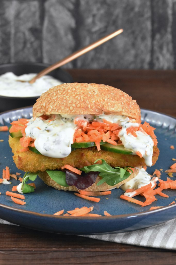 Veganer Fischburger mit Jalapeño-Remoulade auf blauem Teller.