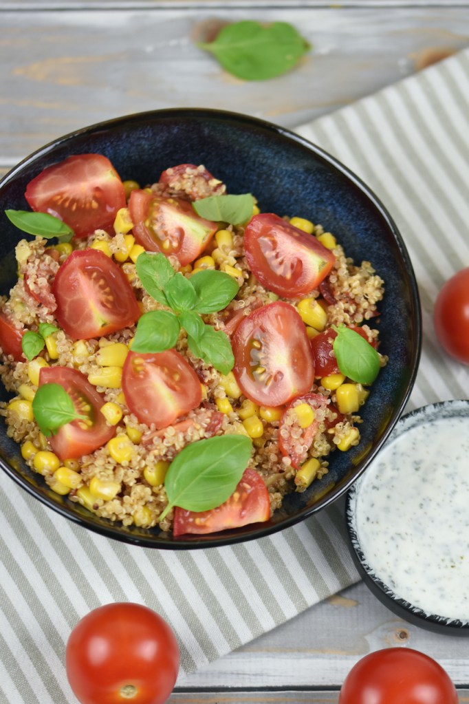 Quinoa Salat mit Avocado in einer schwarzen Schale. Daneben steht in einer kleineren Schale der Minz-Joghurt.
