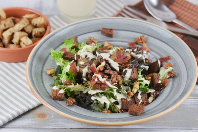 Veganer Caesar Salad mit Pilzen und Walnüssen auf grauem Teller. Hintergrund hell.