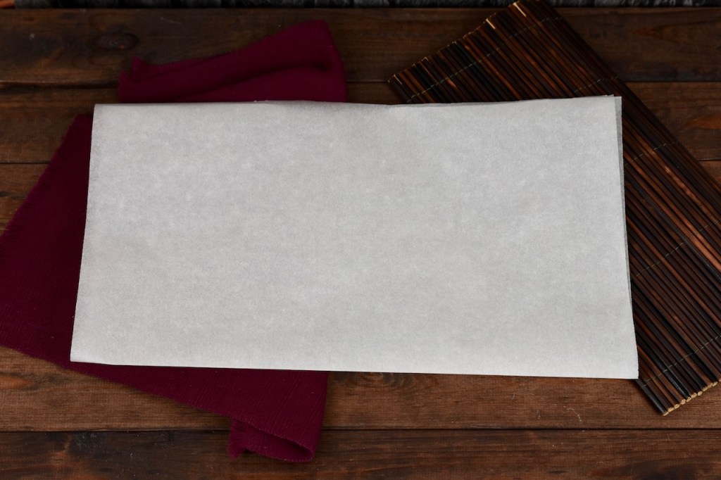 Ein Blatt weißes Backpapier einmal in der Mitte gefaltet. Hintergrund dunkel.