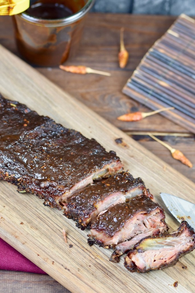 Ribs vom Holzkohlegrill auf Holzbrett. Ein Teil ist angeschnitten. Hintergrund dunkel.