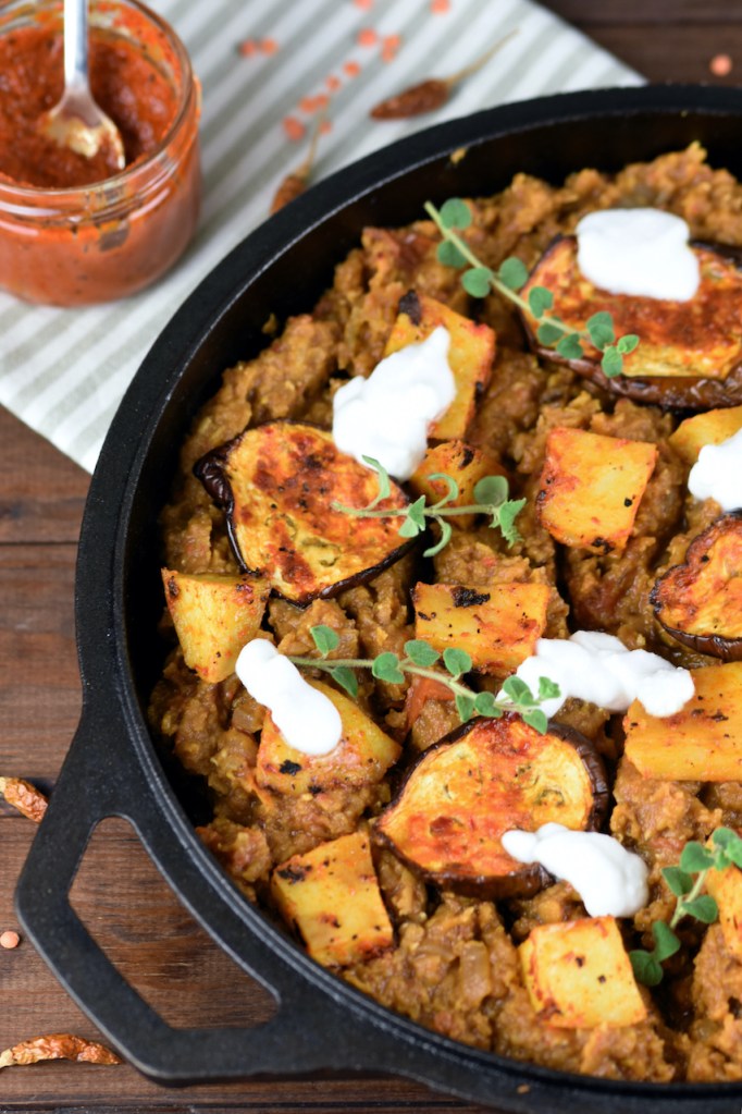Linsen mit Harissa Kartoffeln und Auberginen mit ein paar Klecksen Joghurt dekoriert in einer schwarzen Pfanne aus Gusseisen.