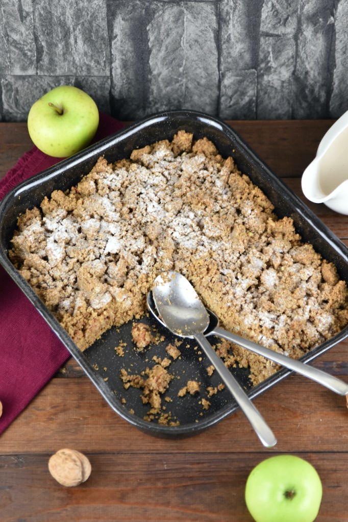Apple Crumble mit Walnüssen und Haferflocken in einer Auflaufform. Hintergrund dunkel.