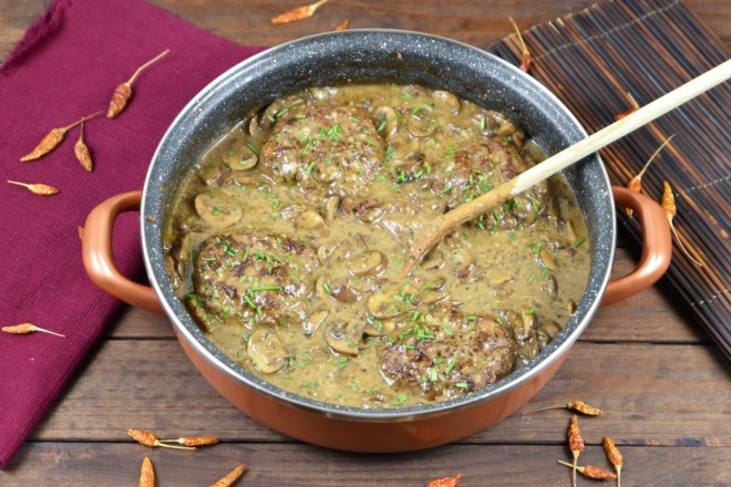Frikadellen aus dem Backofen in cremiger Pilzsauce in einer tiefen Pfanne. Hintergrund dunkel.