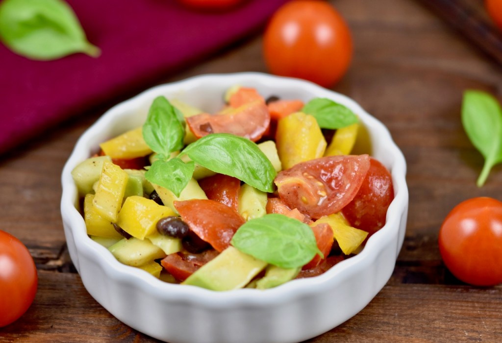 Bunter Avocado-Salat mit Tomaten in weißer Schale. Dekoriert mit Basilikum. Hintergrund dunkel