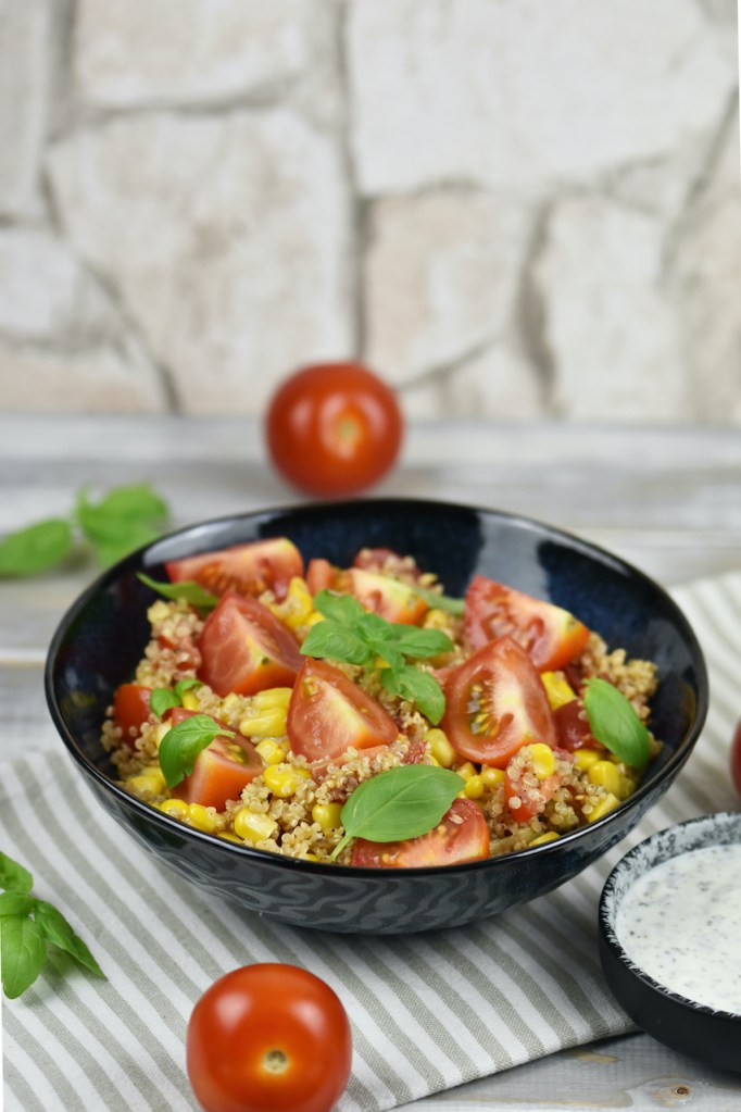 Quinoa Salat mit Avocado in einer schwarzen Schale. Daneben steht in einer kleineren Schale der Minz-Joghurt.