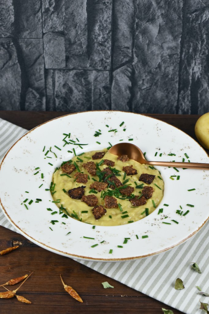 Cremige Kartoffel-Lauch-Suppe in einem weißen tiefen Teller. Hintergrund dunkel.