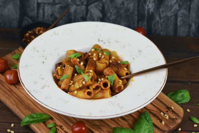 Pasta mit karamellisierten Zwiebeln auf weißem Teller. Hintergrund dunkel.