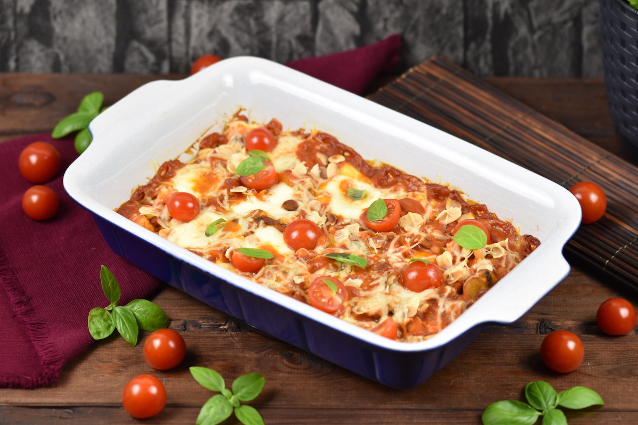 Gnocchi-Auflauf in cremiger Tomatensauce mit Pilzen und Cocktailtomaten in einer Auflaufform. Hintergrund dunkel.