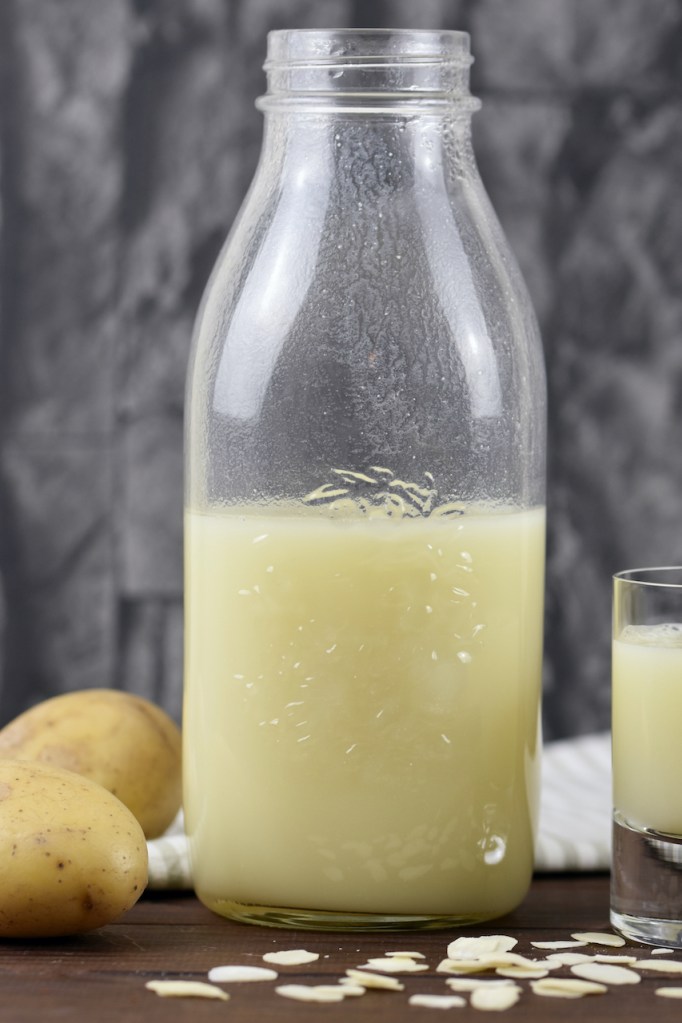 Vegane Milch aus Kartoffeln in einer Glasflasche und einem Glas. Hintergrund dunkel.