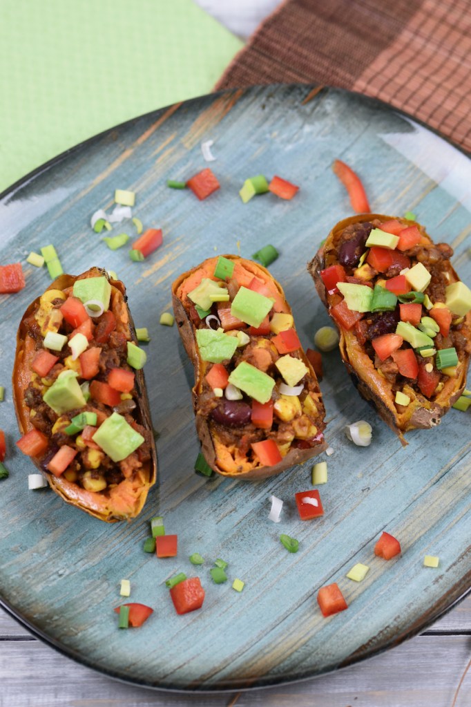 Gefüllte Süßkartoffel auf mexikanische Art dekoriert mit Paprika, Avocado und Frühlingszwiebeln.