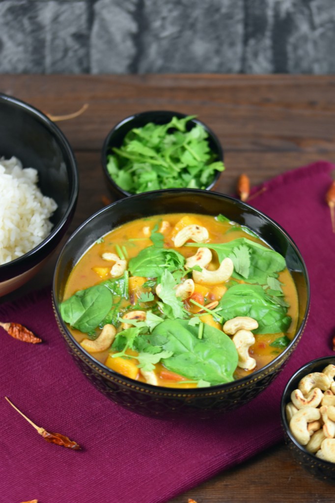 Kürbis-Curry mit Kokosmilch, Kichererbsen und Spinat in einer dunklen Schüssel.