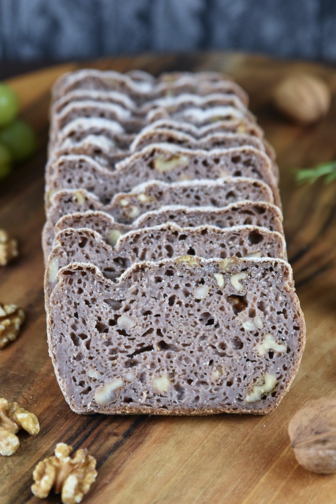 Glutenfreies Walnussbrot aufgeschnitten auf Holzbrett. Hintergrund dunkel.