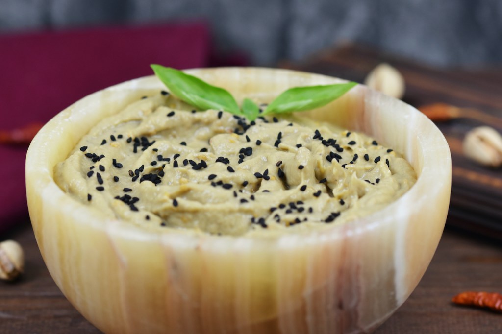 Orientalisches Mutabbal in einer Schale garniert mit Schwarzkümmelsamen und Basilikum. Hintergrund dunkel.