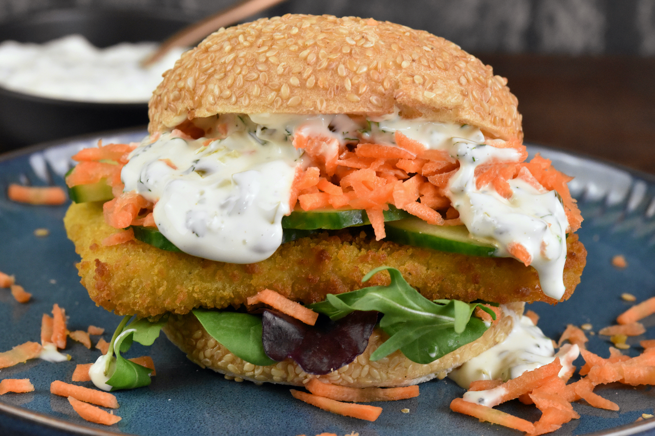 Veganer Fischburger mit Jalapeño-Remoulade auf blauem Teller.