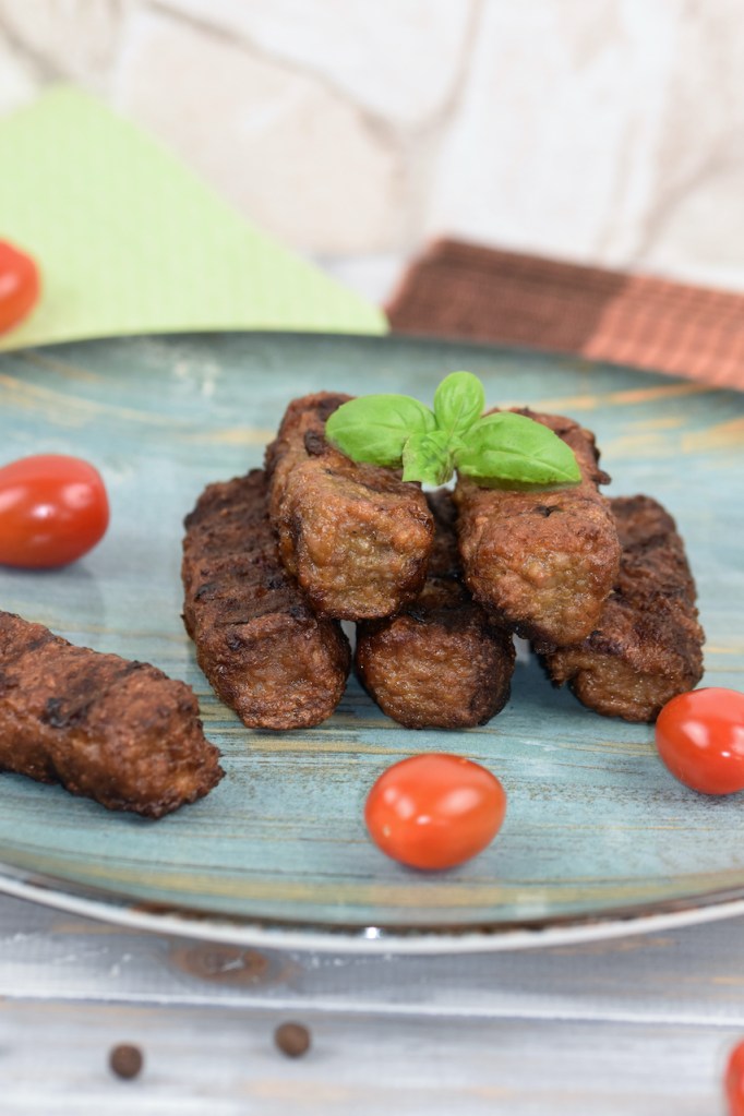 Mehrere Mici oder Mititei auf einem bläulichen Teller. Hintergrund hell.