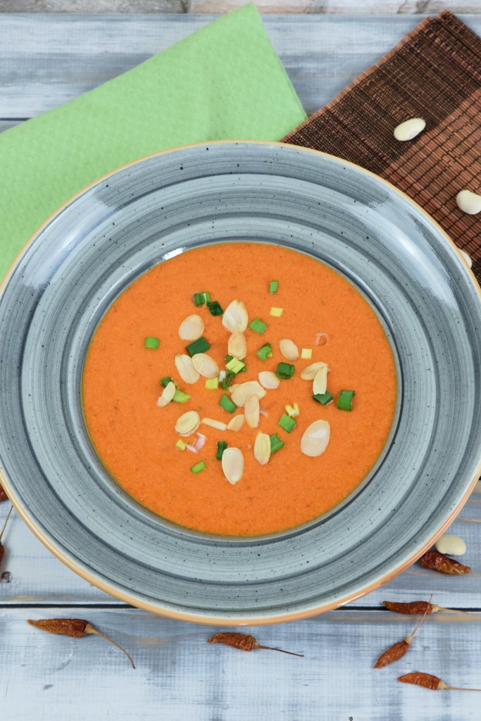 Cremige Paprikasuppe mit Kräutern in einem grauen Teller. Hintergrund hell.