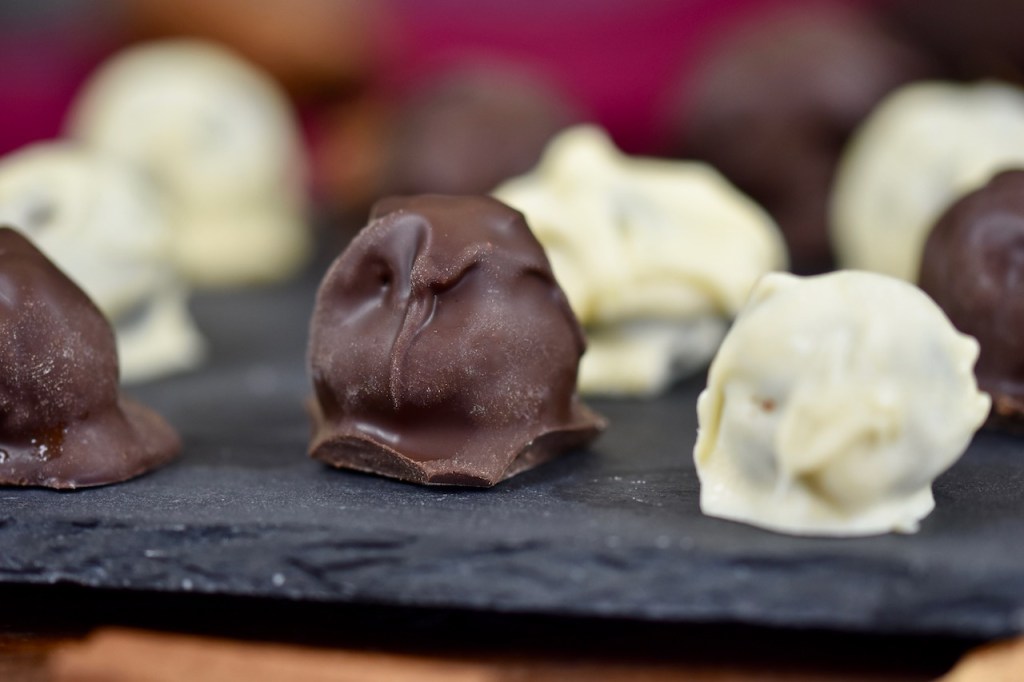 Lakto-Steinpilz-Pralinen mit weißem und dunklem Schokoüberzug auf Schieferplatte. Hintergrund dunkel