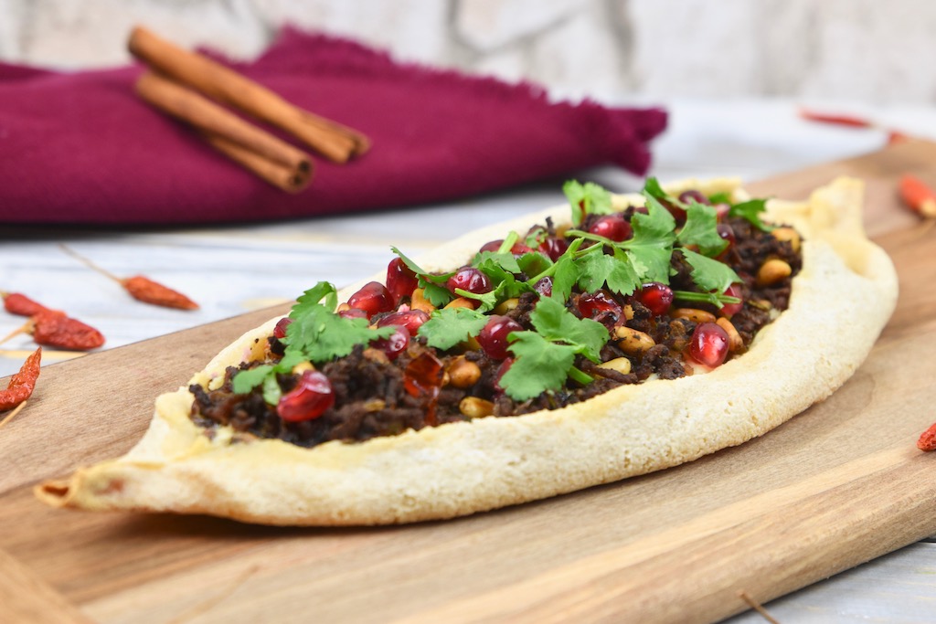 Pide mit Zimt-Hackfleisch, garniert mit Koriandergrün, auf einem Holzbrett.