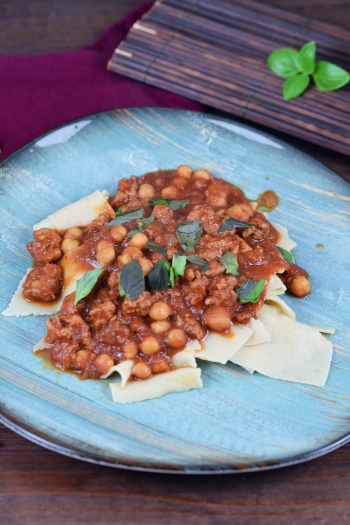 Pasta mit Salsiccia und Kichererbsen auf blauem Teller. Hintergrund dunkel.